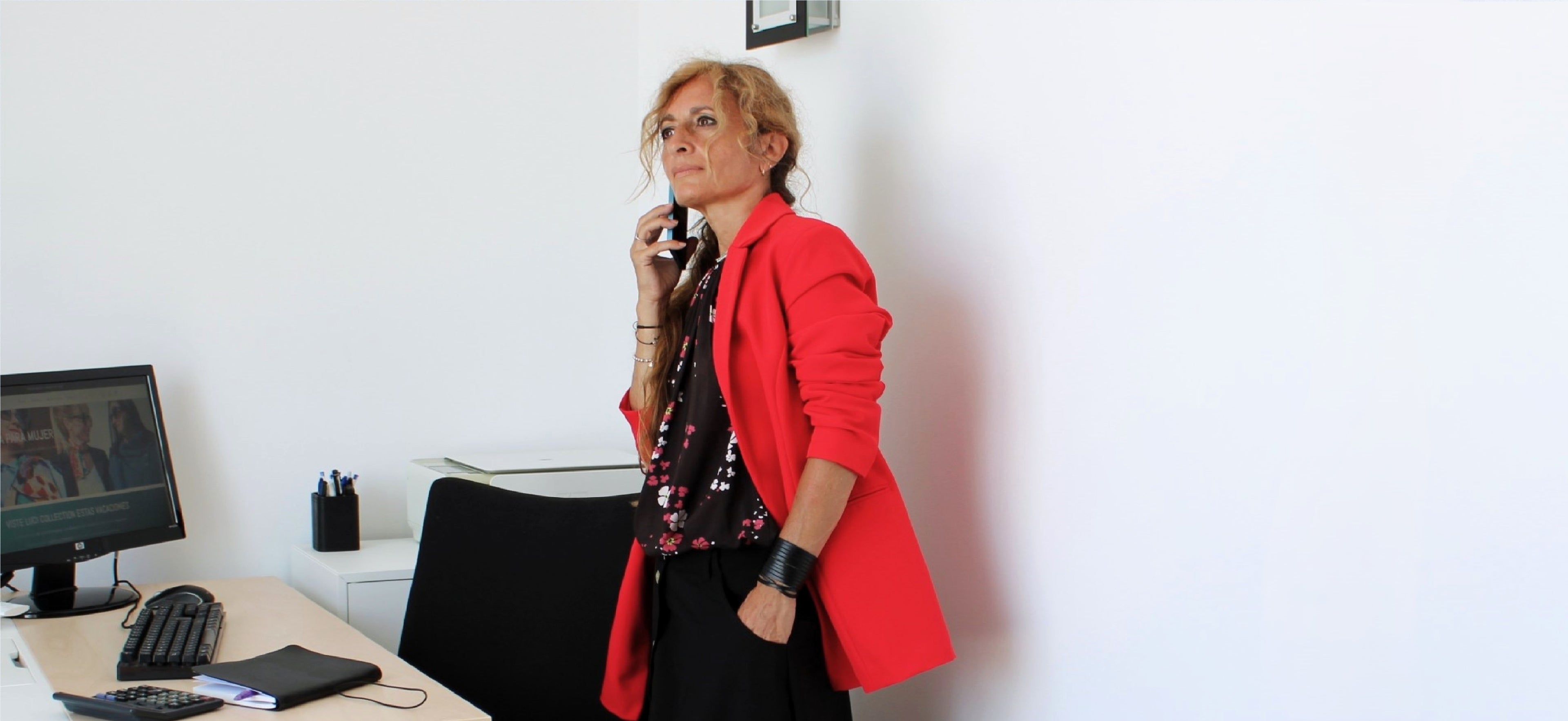 Mujer elegante trabajando en su oficina con americana roja, blusa floreada y falda negra de Luci Collection